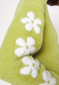 Manche de pull vert doux avec de grands motifs floraux blancs et duveteux en rangée le long du bras.