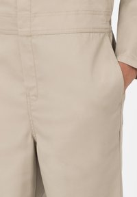 Mono utilitario beige con corte recto, que presenta costuras reforzadas, bolsillos laterales y una suave textura de mezcla de algodón.