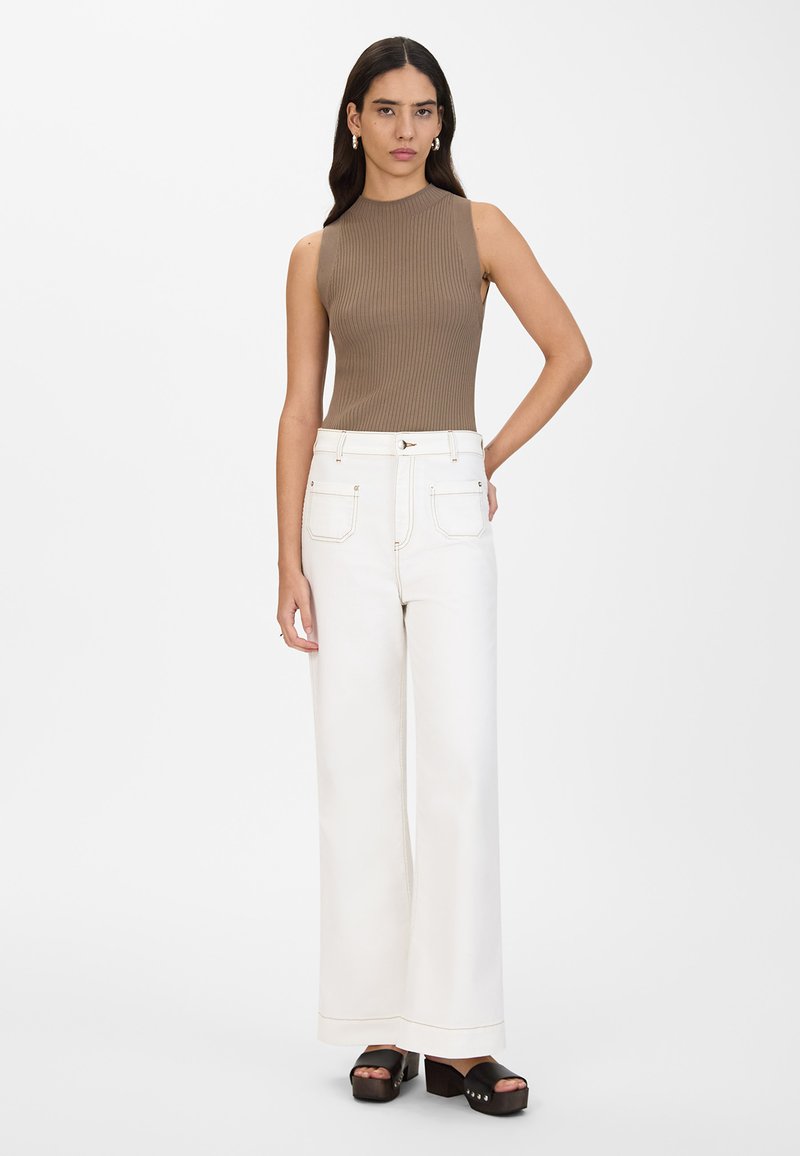 Brun ribbet uten ermer topp kombinert med hvite vide bukser; plattform svarte sandaler med dekorative detaljer; minimalistisk bakgrunn.