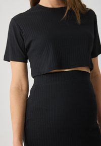 Μαύ�ρο ριγέ σετ δύο τεμαχίων με cropped τοπ με κοντά μανίκια και φούστα με ψηλή μέση, και οι δύο με υφή υφάσματος.