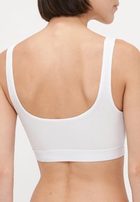 Valkoinen ribbattu bralette, jossa on leveät hihnat ja matala scoop-takaosa. Ominaisuuksiin kuuluu teksturoitu kangas ja logopainettu elastinen nauha alareunassa.