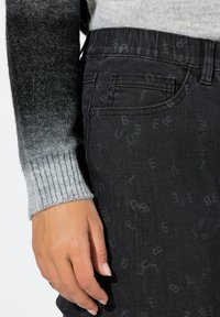 Černé džínové kalhoty s jemným celoplošným vzorem, doplněné šedým žebrovaným svetrem s přechodovým efektem.