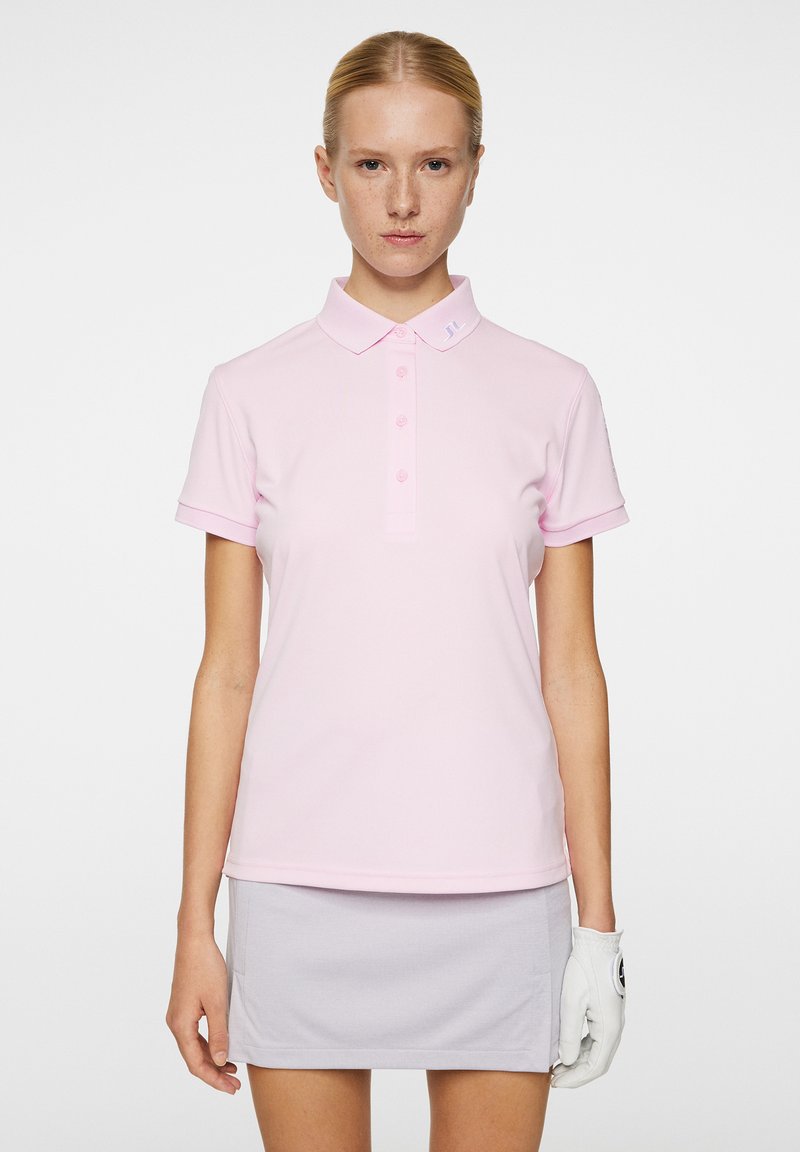 Rosa polo-shirt med klassisk krave, tre-knap lukning og korte ærmer. Bæres med en lys grå nederdel og en hvid golfhandske.
