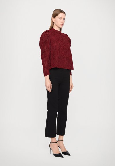 Burgundy knitted sweater with textured design and puffed sleeves, paired with black fitted trousers and black stiletto heels.