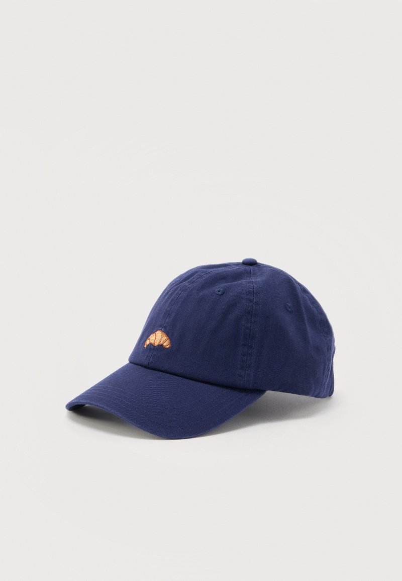 Casquette de baseball bleu marine avec un petit croissant brodé sur le devant, présentée sur une surface gris clair.