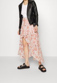 Jupe midi florale en rose pâle, avec un ourlet volanté et des accents orange. Associée à une veste en cuir noire et des sandales noires à clous.