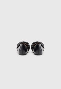 Pantofi slip-on din piele neagră, cu un accent de lanț împletit pe marginea superioară și un profil joasă. Textură netedă, cu un design cu vârf rotund.