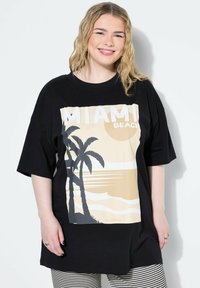 Mustat ylisuuret T-paidat, joissa on graafinen printti palmupuista ja auringonlaskusta sekä teksti "MIAMI BEACH" valkoisissa ja beigen sävyissä.