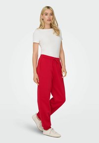 Czerwone dresy ze sznurkiem w pasie i bocznymi kieszeniami, połączone z dopasowanym białym t-shirtem z krótkim rękawem i białymi trampkami.