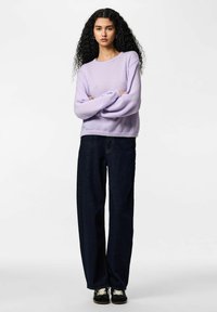 Gaiši lavandas krāsas adīts džemperis ar garām piedurknēm un apaļu kakla izgriezumu; kombinēts ar tumši ziliem platām biksēm un melnām sporta kurpēm. Teksturēts materiāls.