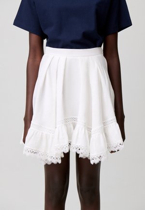 Top blu navy abbinato a una gonna plissettata bianca con bordatura in pizzo e orlo arricciato, indossato da una persona con la pelle scura.