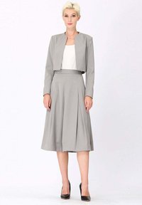 Veste grise ajustée avec un design cropped, assortie à une jupe midi plissée. Texture lisse et lignes simples et épurées. Escarpins noirs.