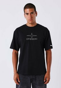 Camiseta de algodón negra con mangas cortas, que presenta un diseño gráfico con brillantina plateada en el centro y un acento blanco en la manga.