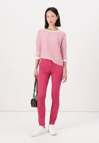 Top de manga larga a rayas rosa y blanco con escote redondeado, combinado con pantalones rosa de corte slim. La modelo lleva zapatillas blancas y sostiene un bolso negro.