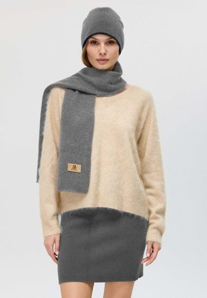 Beige fluffy sweater, grey scarf, and matching hat. The outfit features a color-block design with a smooth texture and a logo patch on the scarf.