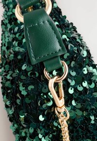 Sac à main vert en sequins avec une sangle en cuir et des finitions dorées, mettant en avant une surface texturée et un fini brillant.