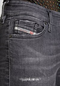 Jeans de mezclilla gris con un bolsillo desgastado que presenta una etiqueta tejida. La tela parece suave, con una ligera textura y un sutil desvanecimiento.