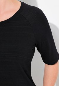 Top negro de manga corta con cuello redondo y tela texturizada, que destaca variaciones sutiles en el tono y un corte relajado.