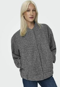Grå, överdimensionerad bomberjacka med en texturerad tyg, ståkrage och framknäppning, ihop med blå denimjeans.