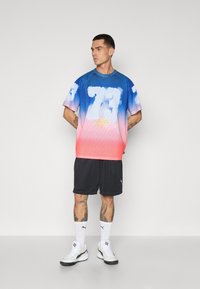 T-shirt à manches courtes dégradé bleu et rose avec un grand numéro blanc 73, en tissu mesh et col rond sportif, associé à un short noir.