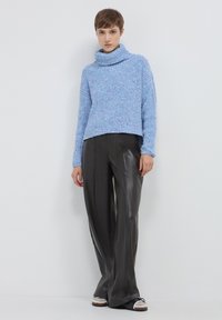 Maglione a collo alto di un azzurro chiaro con texture, dal taglio rilassato, abbinato a pantaloni in pelle nera su misura, caratterizzati da una linea dritta.