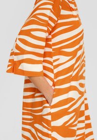 Gestreiftes Kleid in Orange und Weiß mit lockerer Passform, kurzen Ärmeln und seitlichen Taschen, aus leichtem Stoff gefertigt.