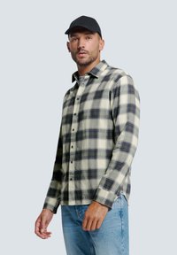 Langärmliges karierter Hemd in Creme und Marineblau mit Knöpfen, ausgestattet mit einem klassischen Kragen und strukturiertem Stoff. Kombiniert mit hellblauen Jeans.
