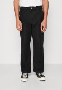 Zwarte cargobroek met een relaxte pasvorm, voorzien van zijzakken en een platte voorkant. G gedragen met zwarte high-top sneakers en een wit T-shirt.