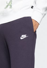 Bílá mikina s kapucí a zelenou grafikou, tmavě šedé tepláky s bílým logem Nike, vyrobené z měkké bavlny.