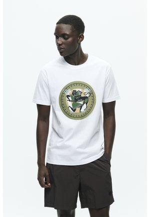 White cotton t-shirt featuring a circular graphic with green and black designs, complemented by dark shorts and a minimalistic style.
