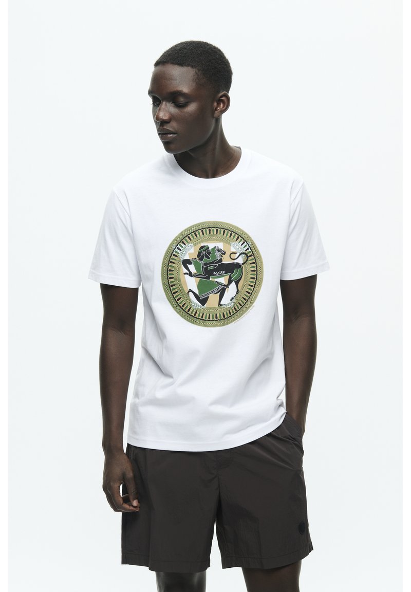 White cotton t-shirt featuring a circular graphic with green and black designs, complemented by dark shorts and a minimalistic style.