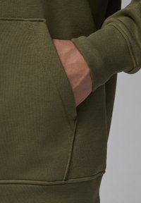 Felpa verde oliva con tasca a marsupio e polsini a coste. Il tessuto è liscio con dettagli di cucitura visibili.