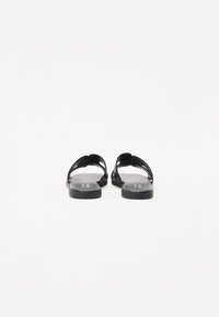 Sandales noires avec une semelle plate, un design ouvert à l'avant et deux sangles courbées. Matériau lisse avec un minimum de détails et sans accents en métal.