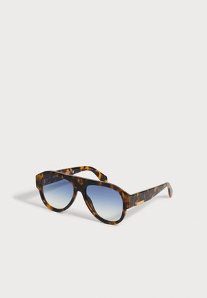 Lunettes de soleil à monture écaille avec verres dégradés bleus, posées sur une surface gris clair, inclinées pour montrer l’avant et le côté.