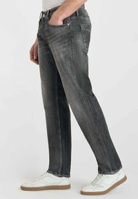 Jean en denim gris avec une coupe droite, taille mi-haute et décoloration subtile. Associé à des baskets blanches, mettant en avant un style décontracté.