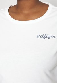 Witte katoenen T-shirt met een ronde hals en geborduurd "Hilfiger" logo in marineblauw aan de linkerkant. Soepele textuur.