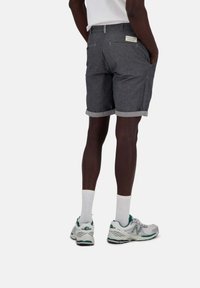 Pantaloni corti grigi con orlo risvoltato, tasche laterali e una tasca posteriore con etichetta del marchio; abbinati a calze bianche e scarpe da ginnastica grigie.