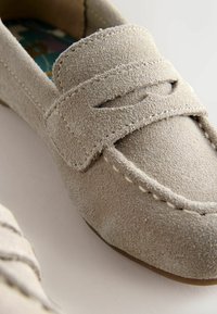 Mocasini din piele întoarsă gri deschis, cu un design cusut, având o curea decorativă peste partea superioară și o căptușeală interioară netedă.