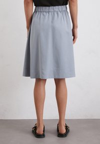 Jupe mi-longue gris clair avec une taille élastique, texture lisse et silhouette légèrement évasée, se terminant par un ourlet près du genou.