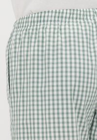Pantalons à carreaux vichy verts et blancs avec une taille élastique, des poches latérales et une texture en coton douce et légère.