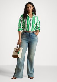 Camisa de botões com riscas verdes e brancas, corte descontraído, combinada com jeans azuis desbotados de perna larga, cinto de couro castanho e saco tote creme com tassel.