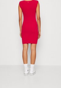 Strakke rode bodycon jurk met korte mouwen, lengte tot de knie, gladde textuur, gedragen met witte sneakers en enkelkousen.