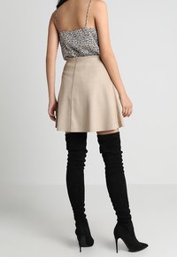 Botas de ante negras por encima de la rodilla, una falda mini beige y una camiseta sin mangas de leopardo con tirantes finos, vistas desde atrás.