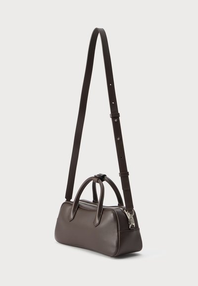 Sac à main en cuir marron foncé avec doubles poignées et une longue bandoulière ajustable, posé sur un fond clair uni.