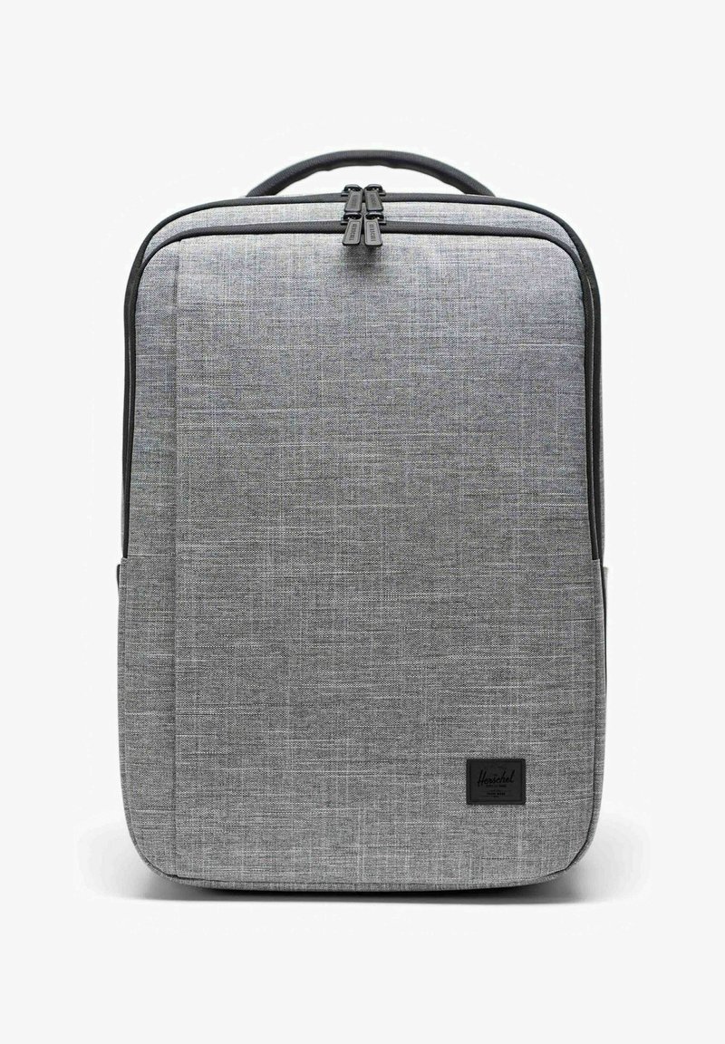 Sac à dos en tissu gris rectangulaire avec tirettes de fermeture éclair noires et une poignée noire, affichant une petite étiquette de marque noire en bas à droite.