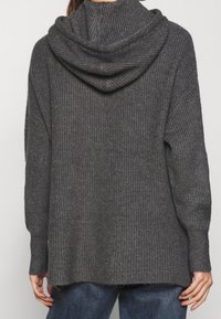 Person, der einen dunkelgrauen gestrickten Hoodie mit langen Ärmeln trägt, von hinten gezeigt, kombiniert mit blauen Jeans.