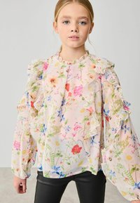 Blommig chiffongblus med volangärmar, prydd med rosa, röda och blå blommor på en ljus bakgrund. Rundad halsringning och genomskinlig textur.