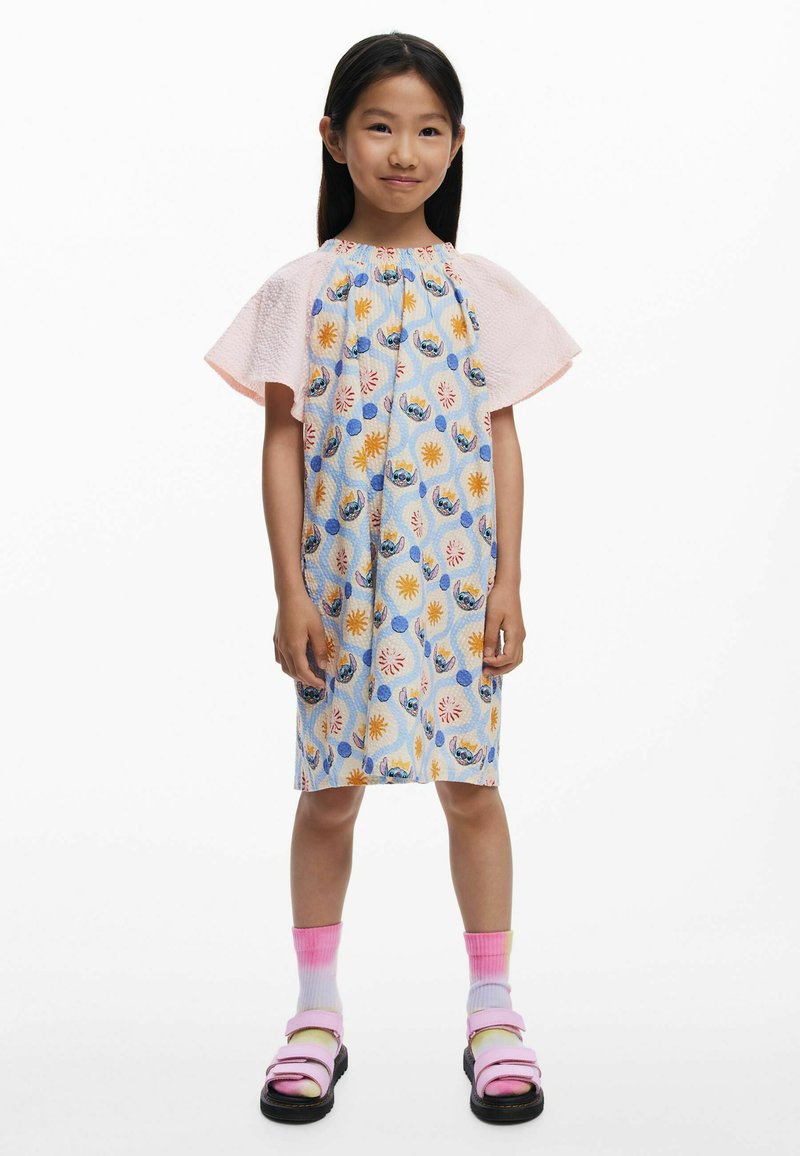 Blumenmuster-Kleid in Blau, Gelb und Pink mit kurzen, rosa texturierten Ärmeln. Kombiniert mit rosa-weißen Verlaufsocken und schwarzen Sandalen.