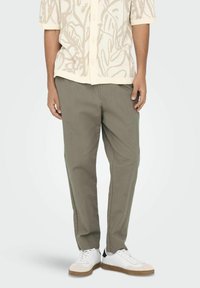 Lettheadde, olivenfarvede bukser med en afslappet pasform, parret med hvide sneakers og en mønstrede, kortærmet beige skjorte.