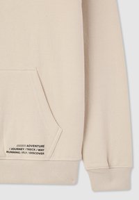 Felpa beige con tasca frontale, polsini e orlo a costine, con dettagli in nero che riportano parole legate all'avventura e all'esplorazione.